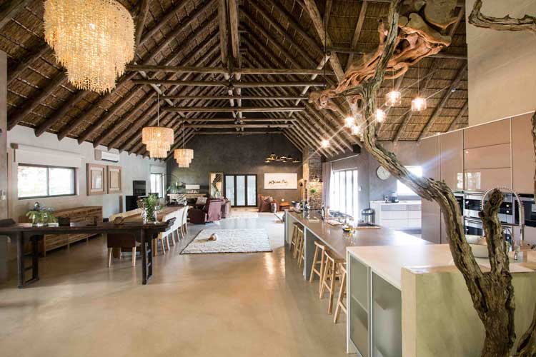 Spacious open-plan living area with thatched ceiling, chandeliers, modern kitchen, and rustic decor