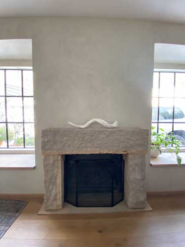 Stone fireplace with rustic mantelpiece, decorative sculpture, and windows on both sides