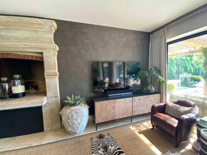 Modern living room with TV unit, stone fireplace, leather armchair, and large window overlooking garden