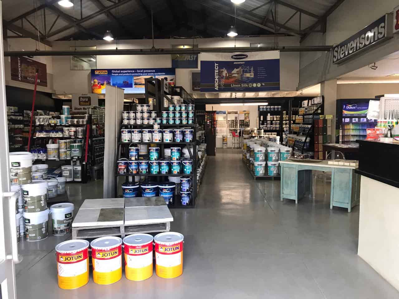 Interior of a paint and hardware store with shelves of paint buckets and products on display.