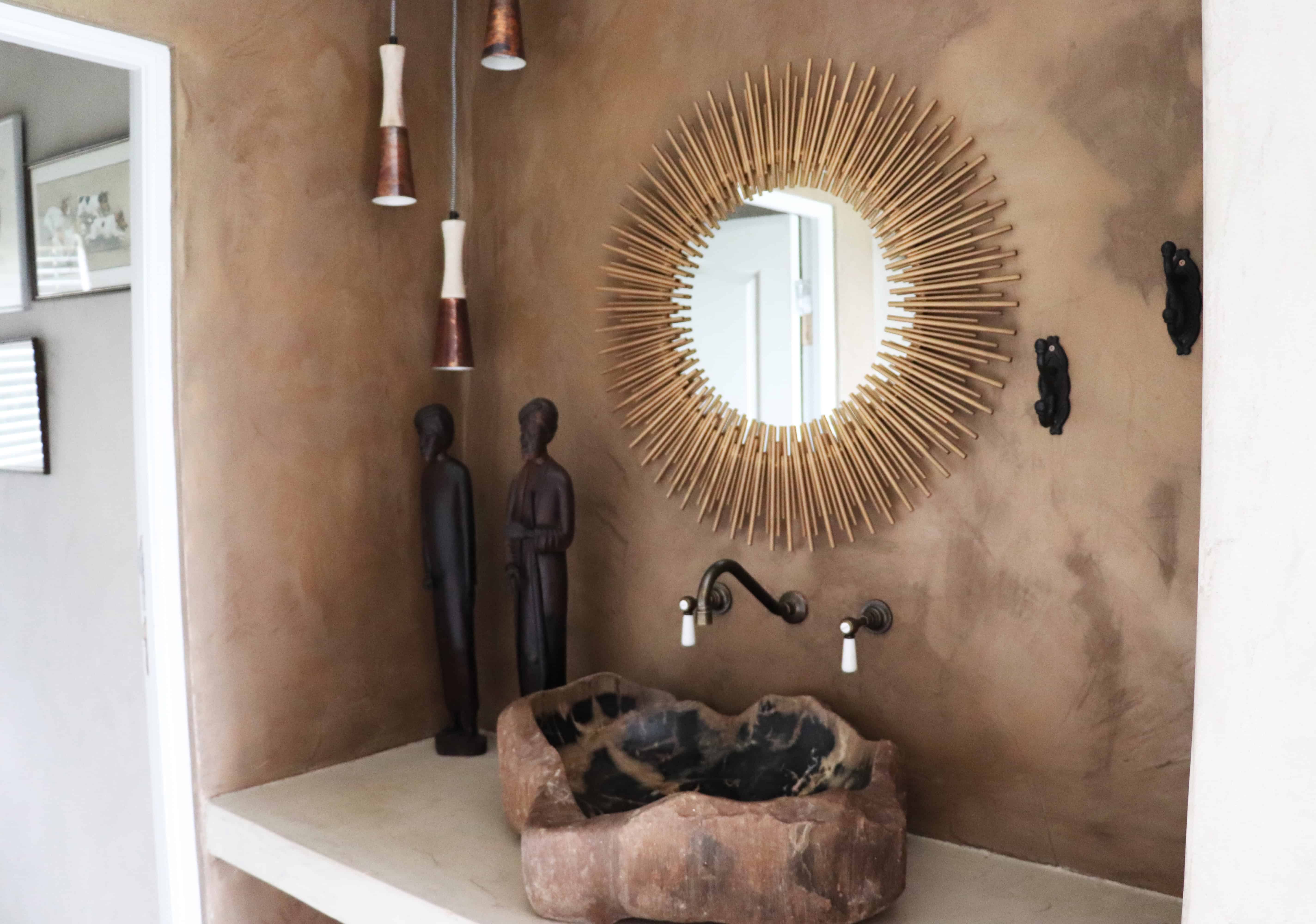 Bathroom with stone sink, round mirror, and artistic wooden decor