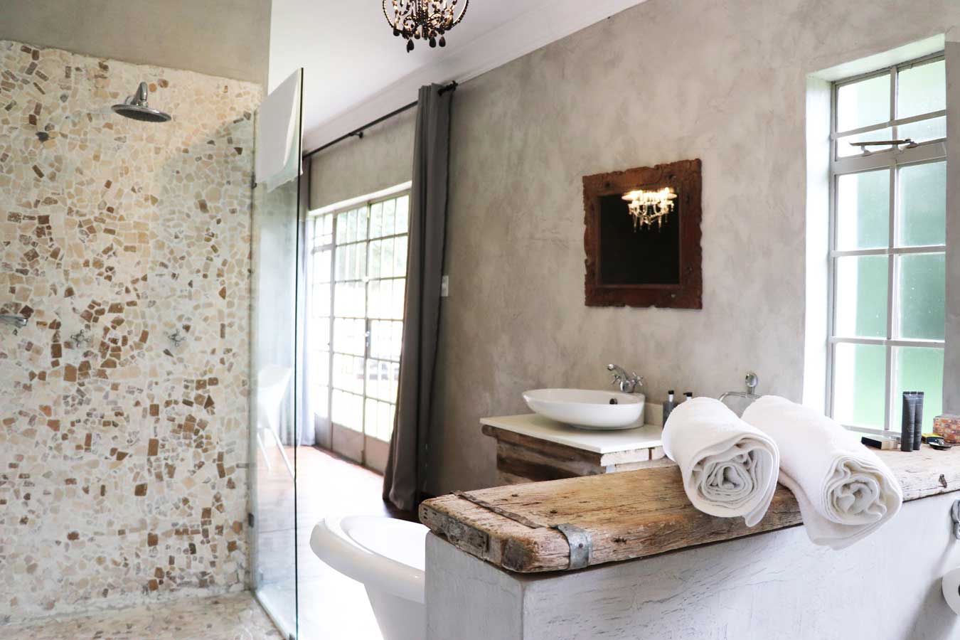Modern rustic bathroom with stone shower wall, rolled white towels, and natural wood accents