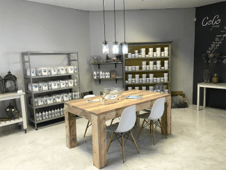 Modern shop interior with wooden table, white chairs, shelves of products, and hanging lights