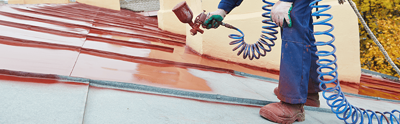 Worker spraying red protective paint on a roof surface