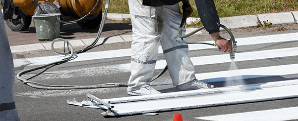 Worker spray painting white road markings on asphalt