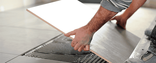 Worker laying ceramic tile onto adhesive on floor