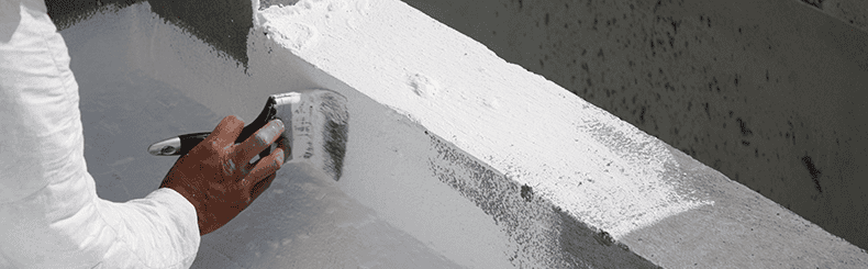 Applying white waterproofing paint with a brush on concrete surface